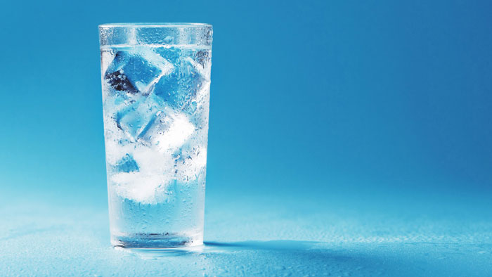 Copo de água potável com cubos de gelo em fundo azul