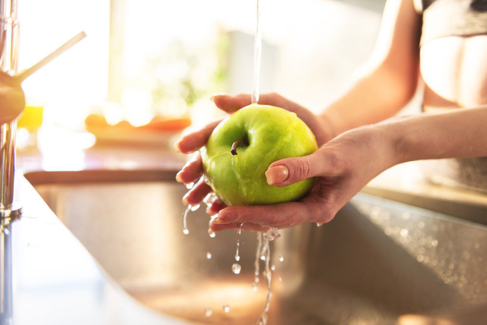 Mãos femininas lavando maçã com água potável