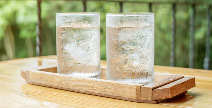 Copos de água gelada, com gelo, em suporte de madeira